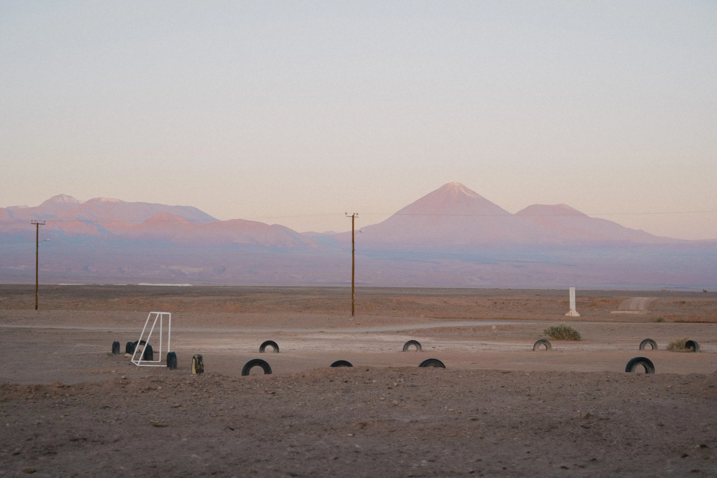 Desert landscape with mountains in the background, power poles, and a small soccer goal with tires in the foreground.