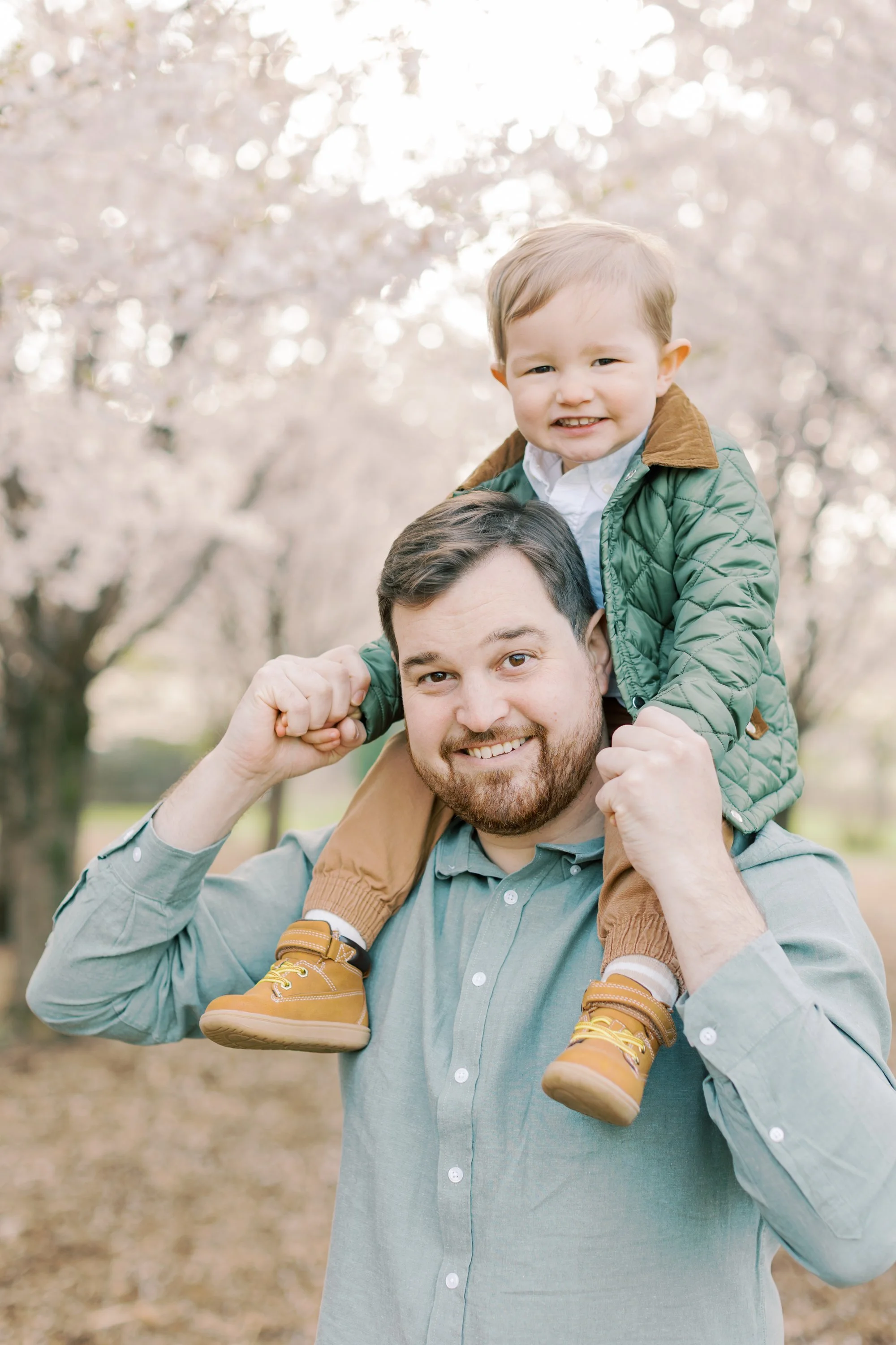 A pregnant mother and her toddler son under cherry blossom trees during a maternity session in Burlington, Ontario.