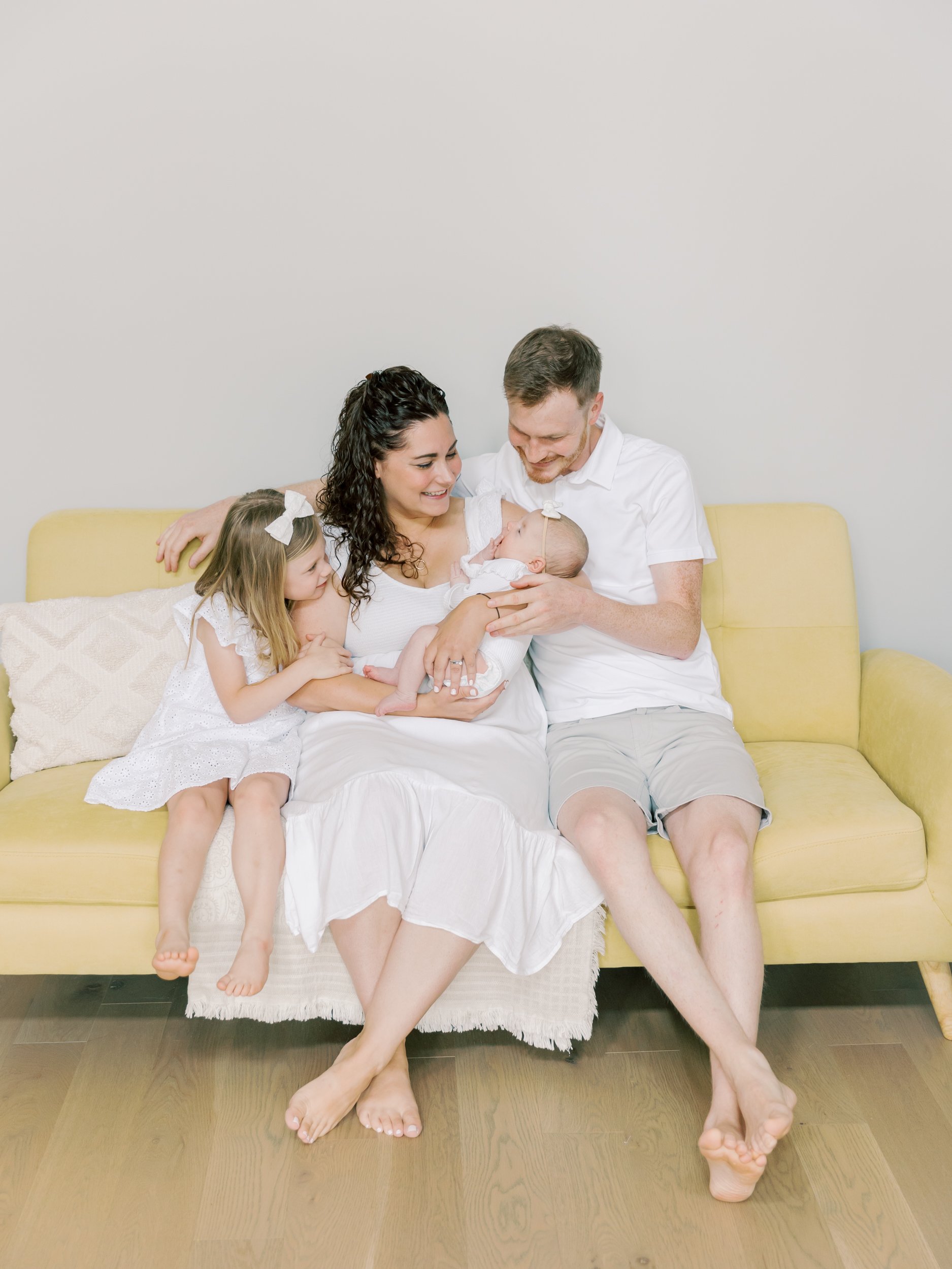 Family holding newborn baby in their sunny living room during a relaxed in-home Burlington Baby Photographer session.