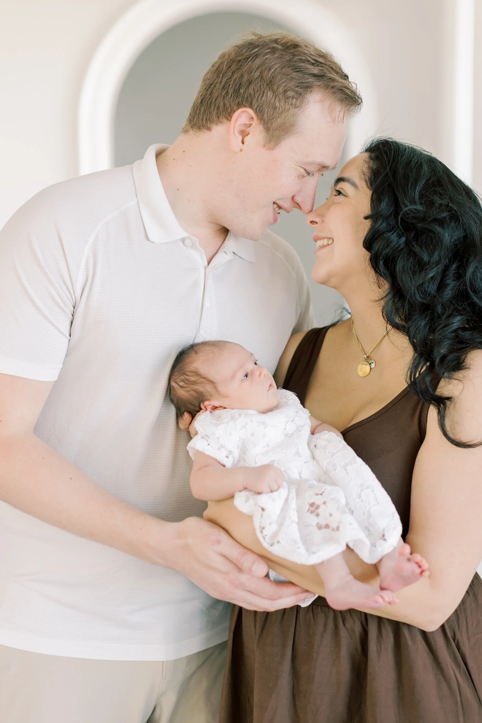 A tiny newborn sleeping soundly in a parent's arms, illustrating a successful, stress-free moment of an in-home shoot.