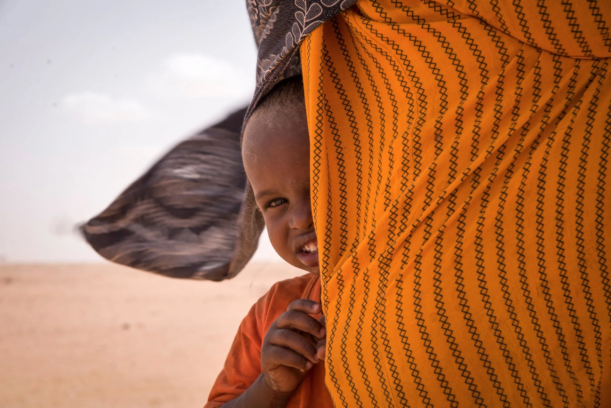 A boy hides behind his mother’s dress during a sandstorm in a remote village in Wajir County, Northern Kenya.