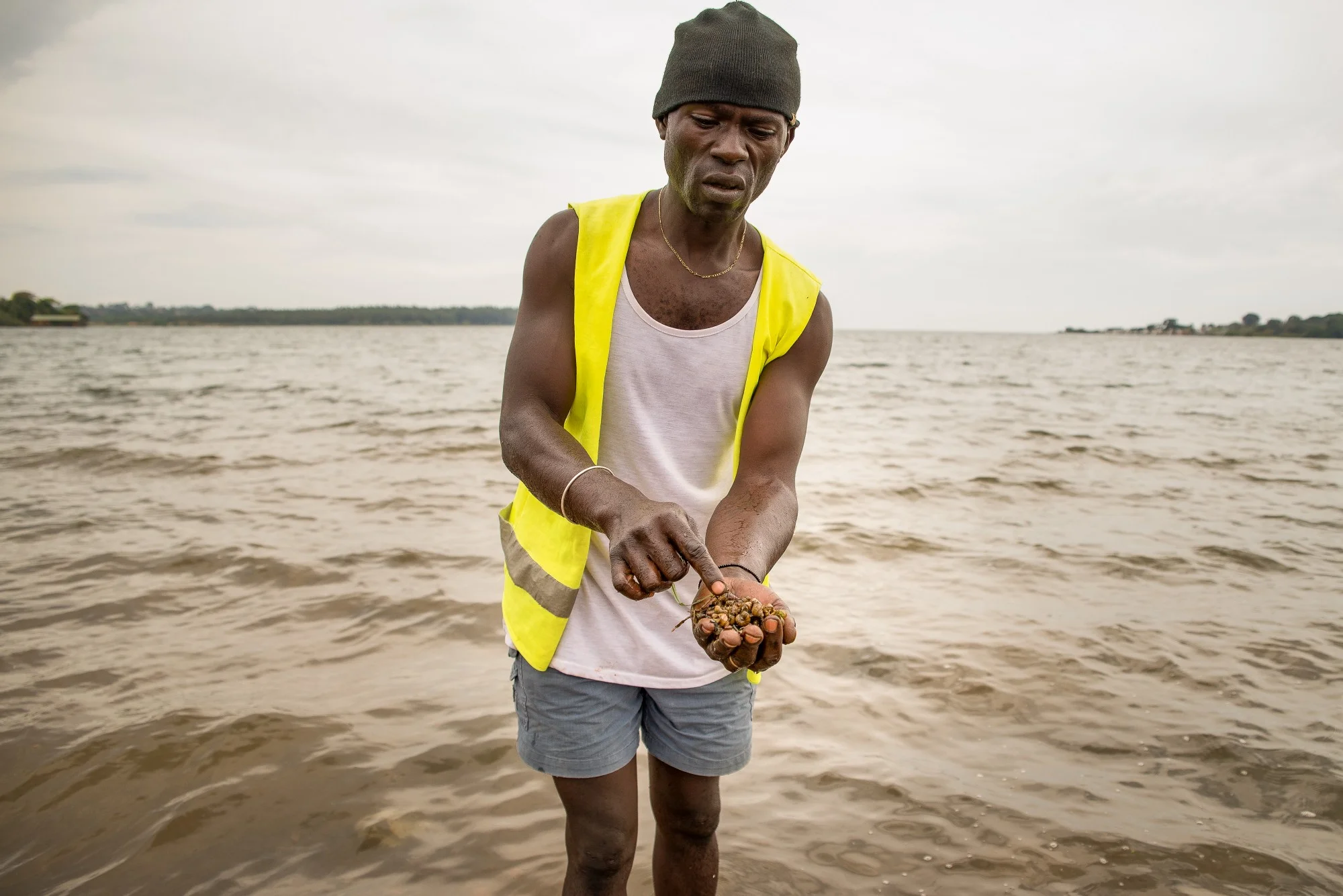 Beach cleaner Bob Shaban with a handful of freshwater snails pulled from the banks of Lake Victoria in Uganda. These small snails often harbor the parasitic flatworm that transmits schistosomiasis. Photo: RTI International/Katie Nelson