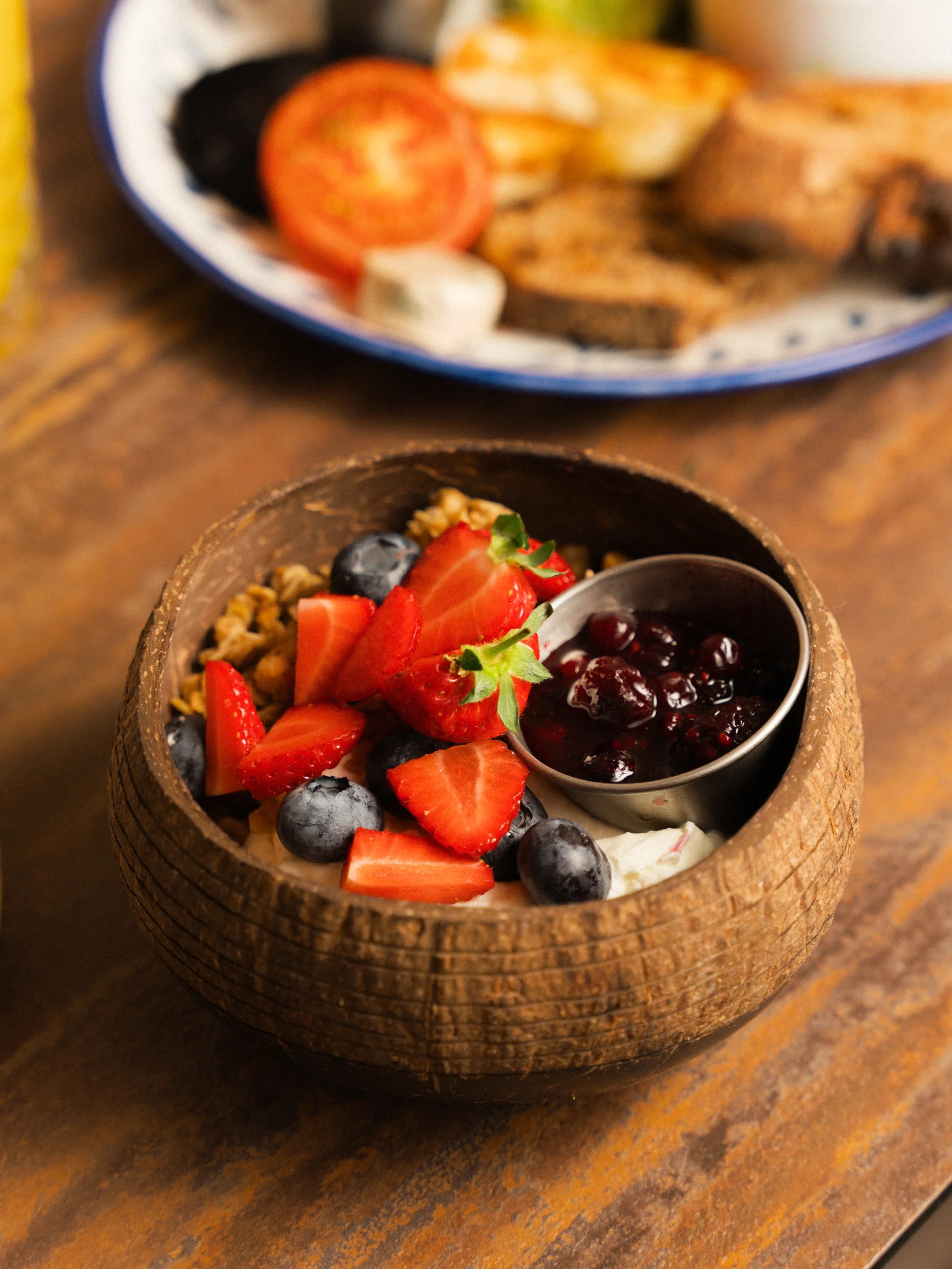 Fruit-topped yogurt bowl with strawberries, blueberries, granola, and berry sauce on a wooden table