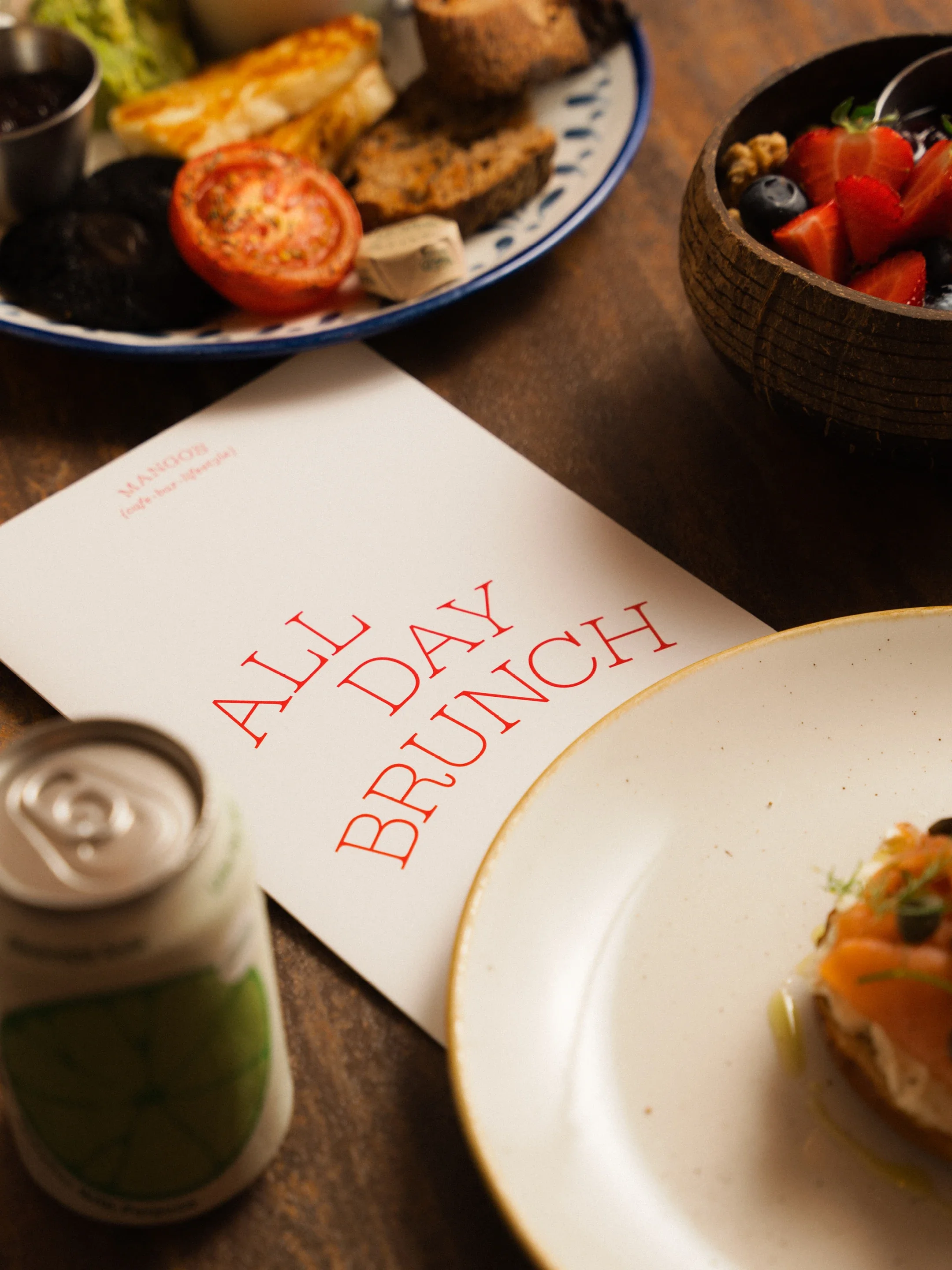 Restaurant table with a vegetable meal, roasted bread, fresh tomato, berries, and a book titled “BREAKFAST LUNCH”.