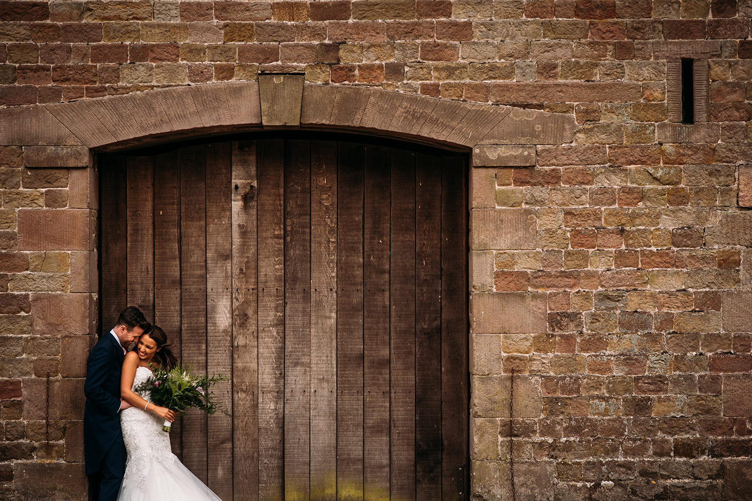  colour photo of bride and groom by barn door 