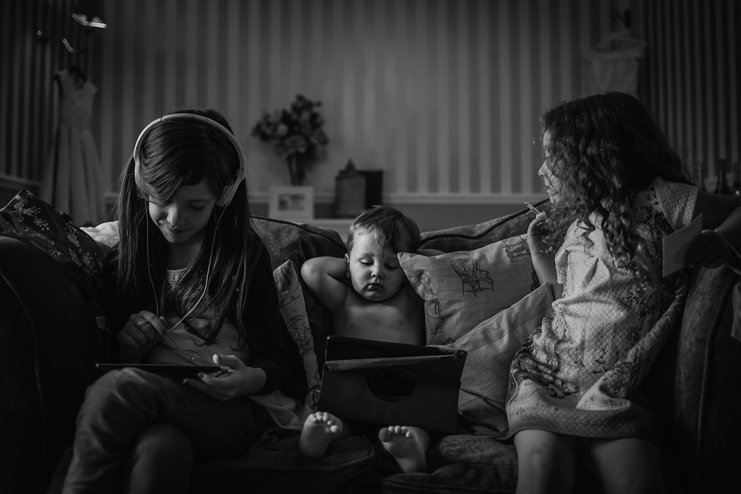  Black and white photo of 3 kids watching ipads on a sofa 