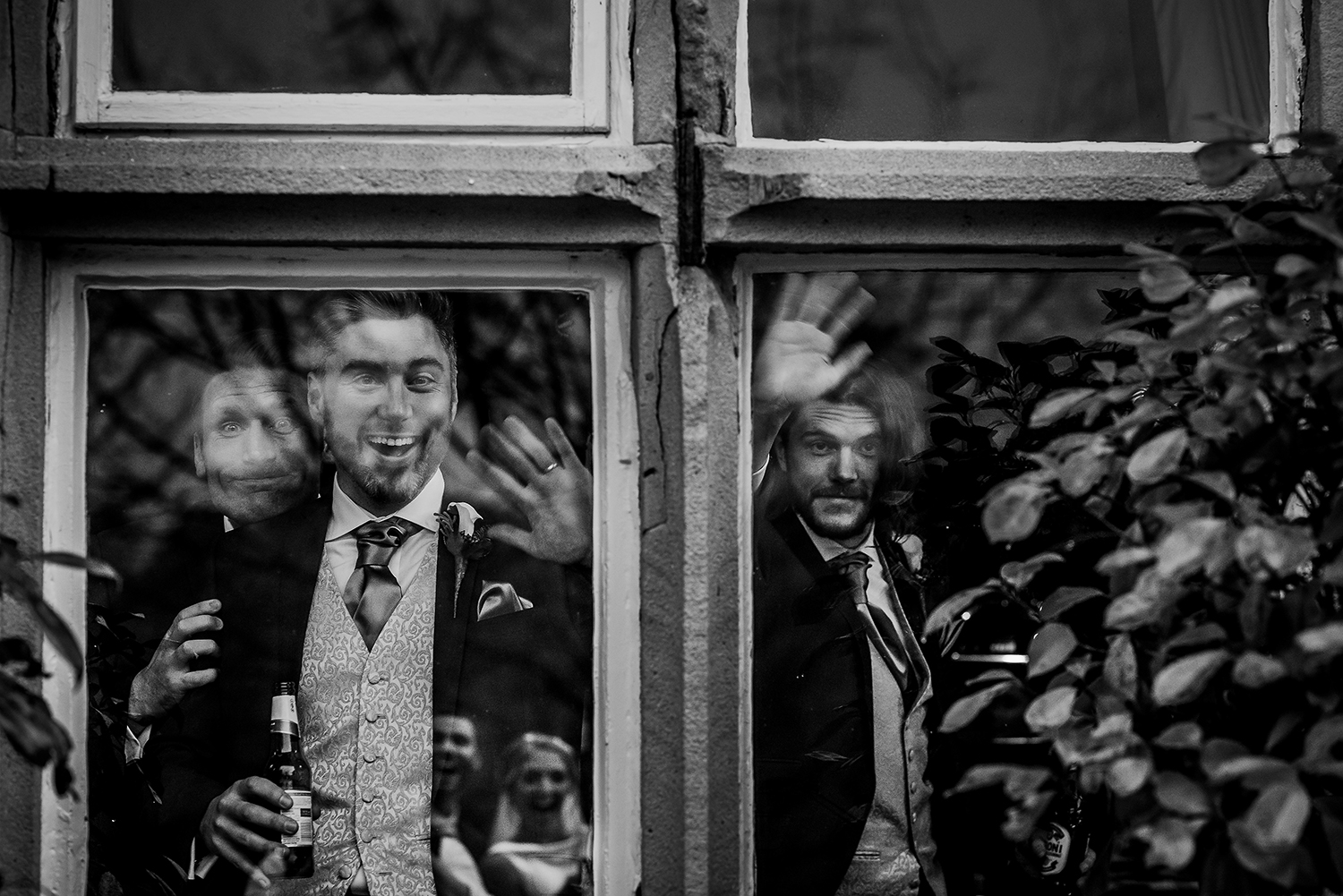  BW photo of guests laughing through the window with bride and grooms reflection 