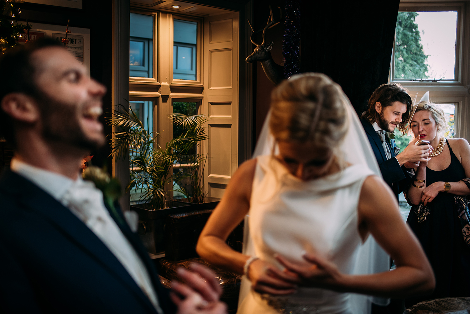  guests looking at phone with bride and groom laughing in the foreground.&nbsp; 