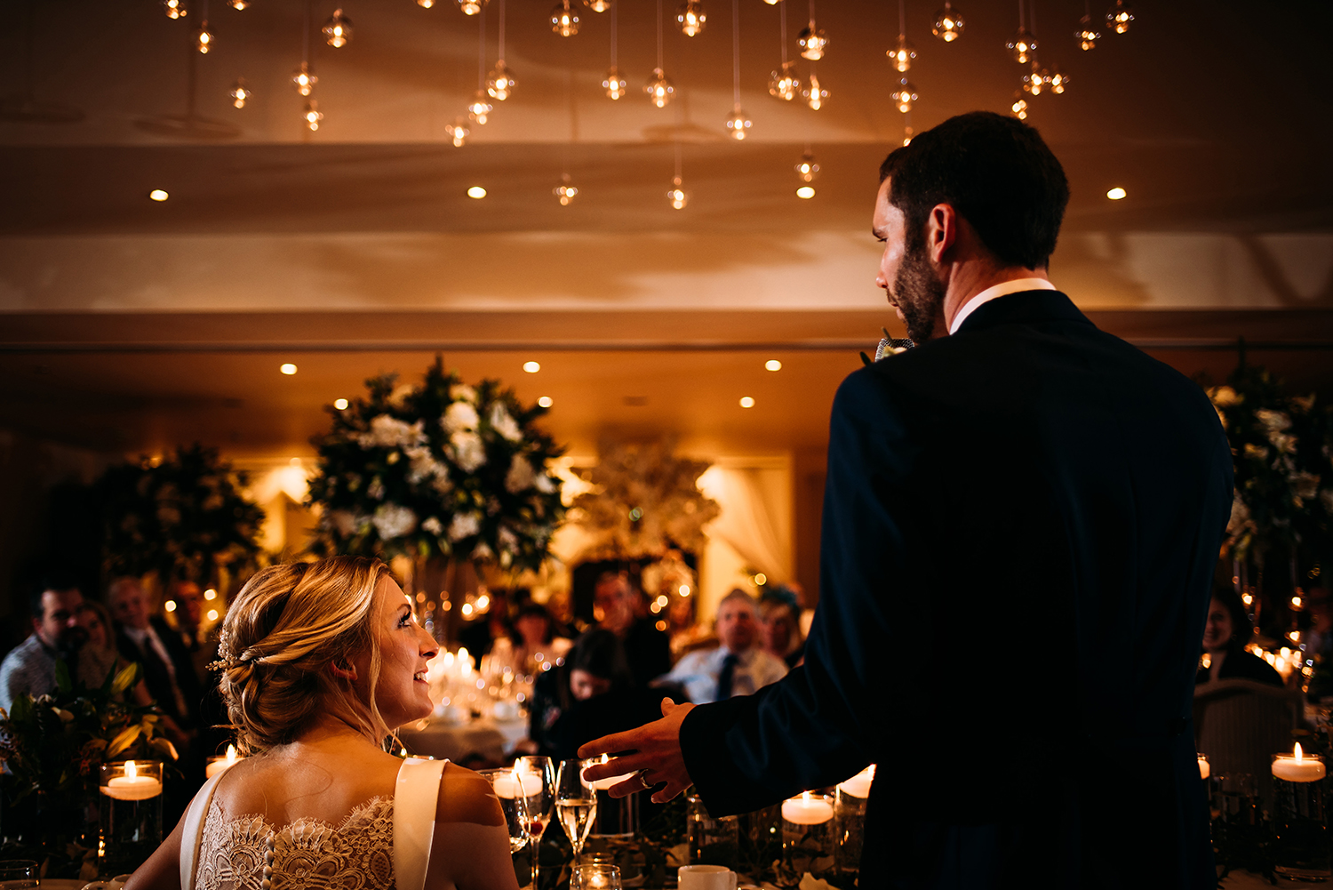  bride and groom during groom speech. Shot from the back - can see guests in shot 