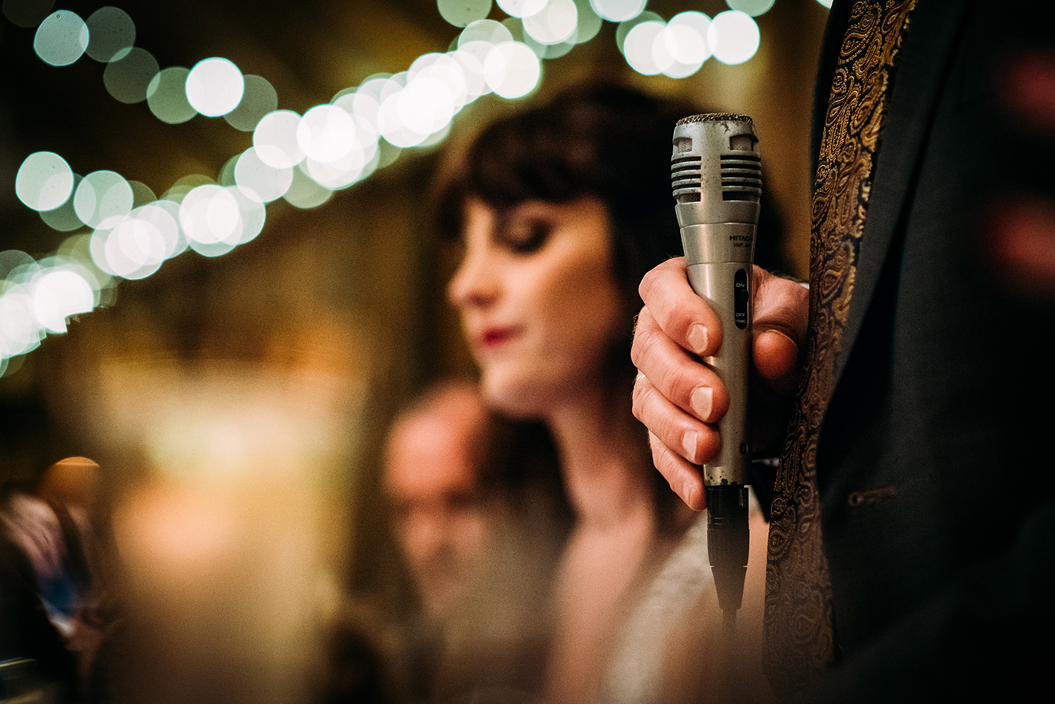 fathers hand holding microphone, bride in the background - soft focus