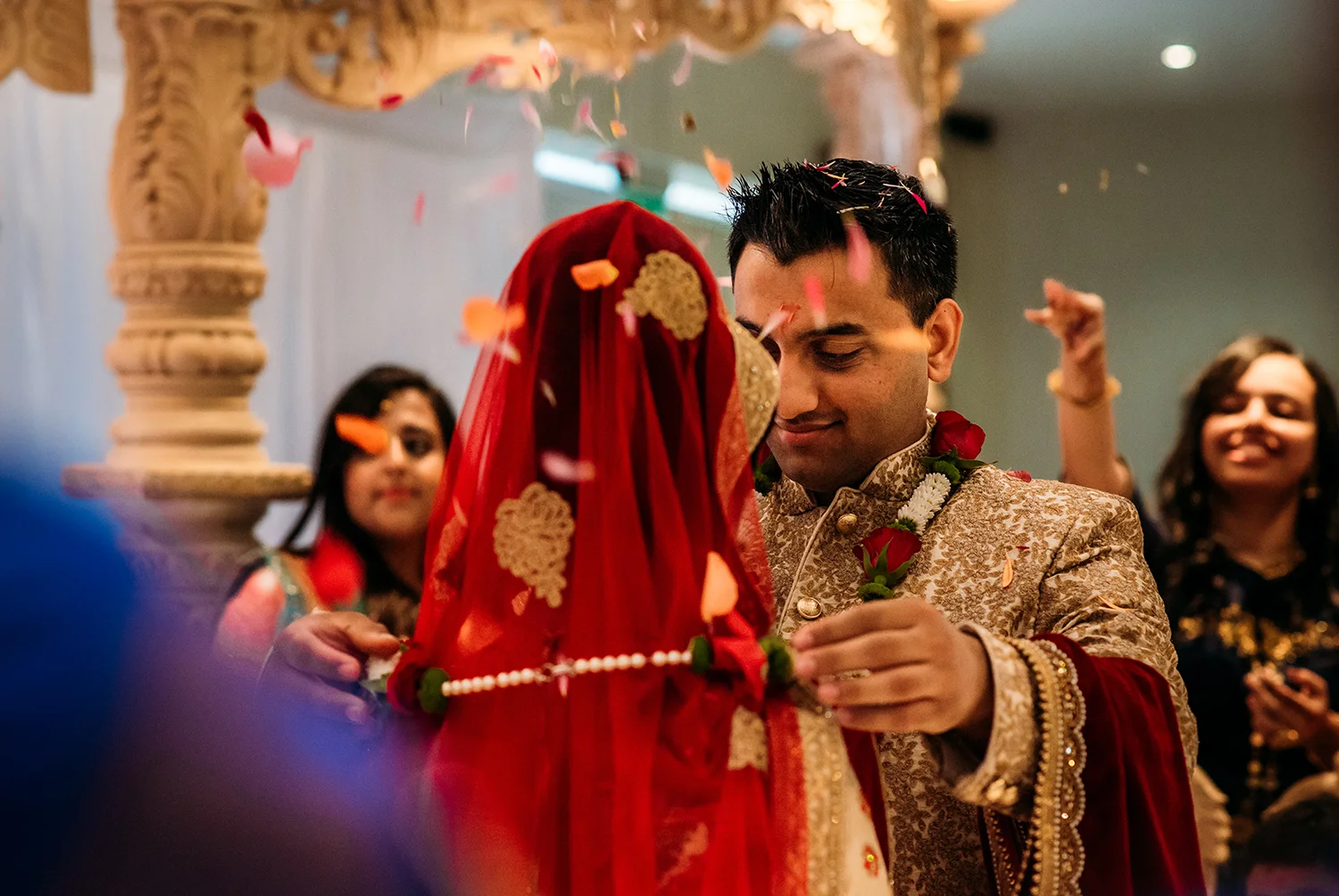 groom putting a necklace on the bride while confetti is thrown at them
