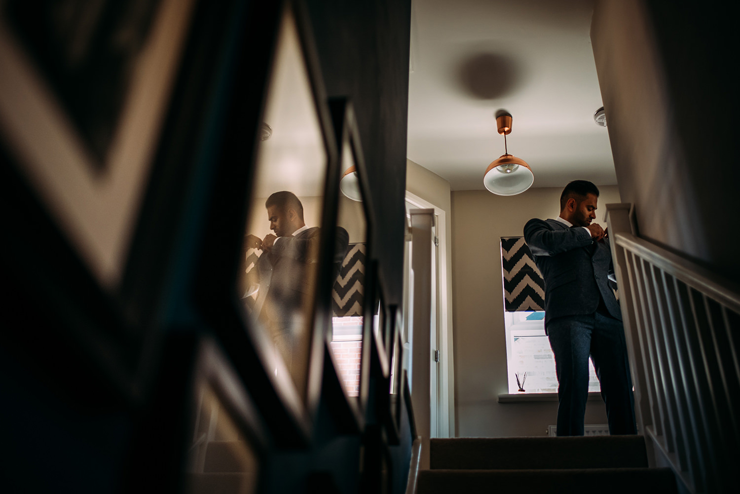  groomsman putting flower on jacket at the top of the stairs with a reflection in the picture frame 
