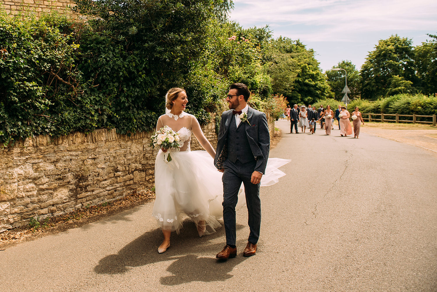  bride and groom walk through the village with their family in the distance 