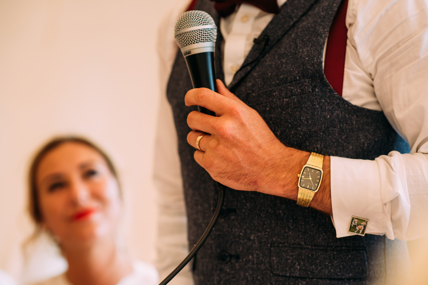  detail of grooms watch and microphone during the speeech with bride looking on in the background 