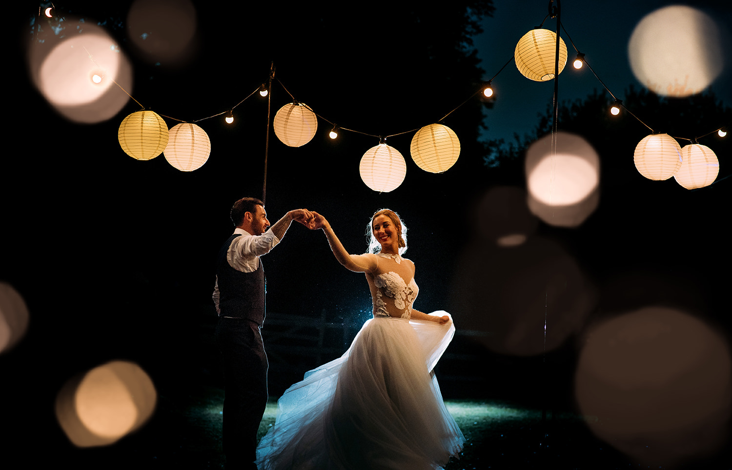  night time image of the bride and groom dancing under lanterns 