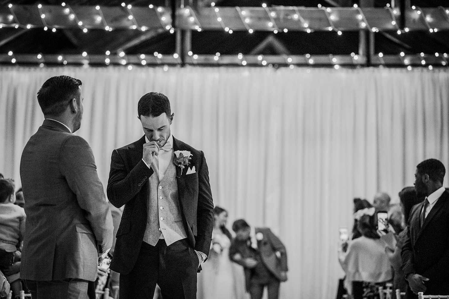 bw photo of nervous groom biting his thumbnail as the bride enters in the background
