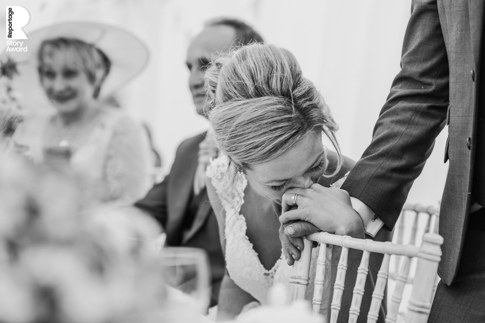 an emotional bride squeezes her husbands hand during his speech. Bw photo