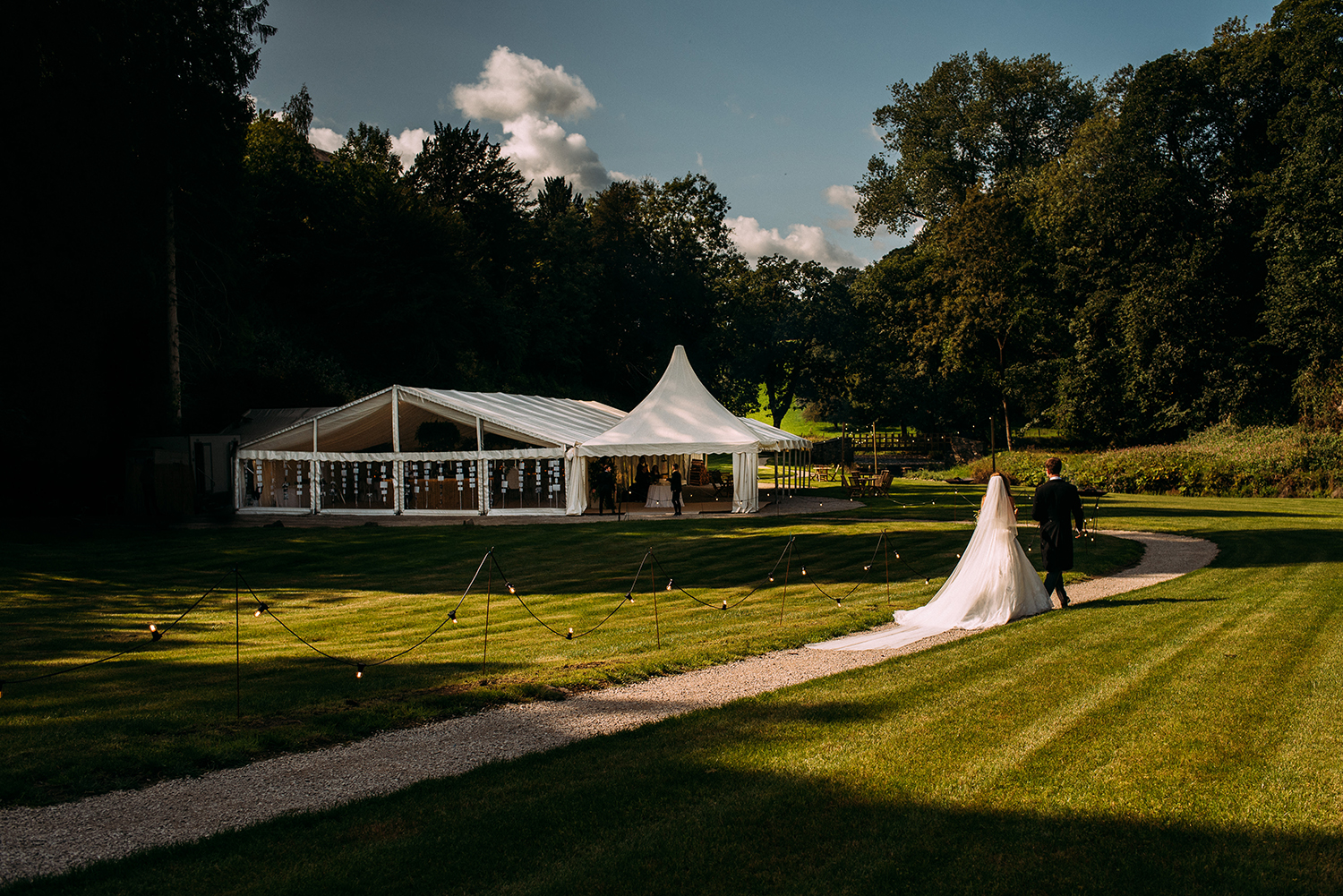  bride and groom walking along a fairy lit path to the marquee 