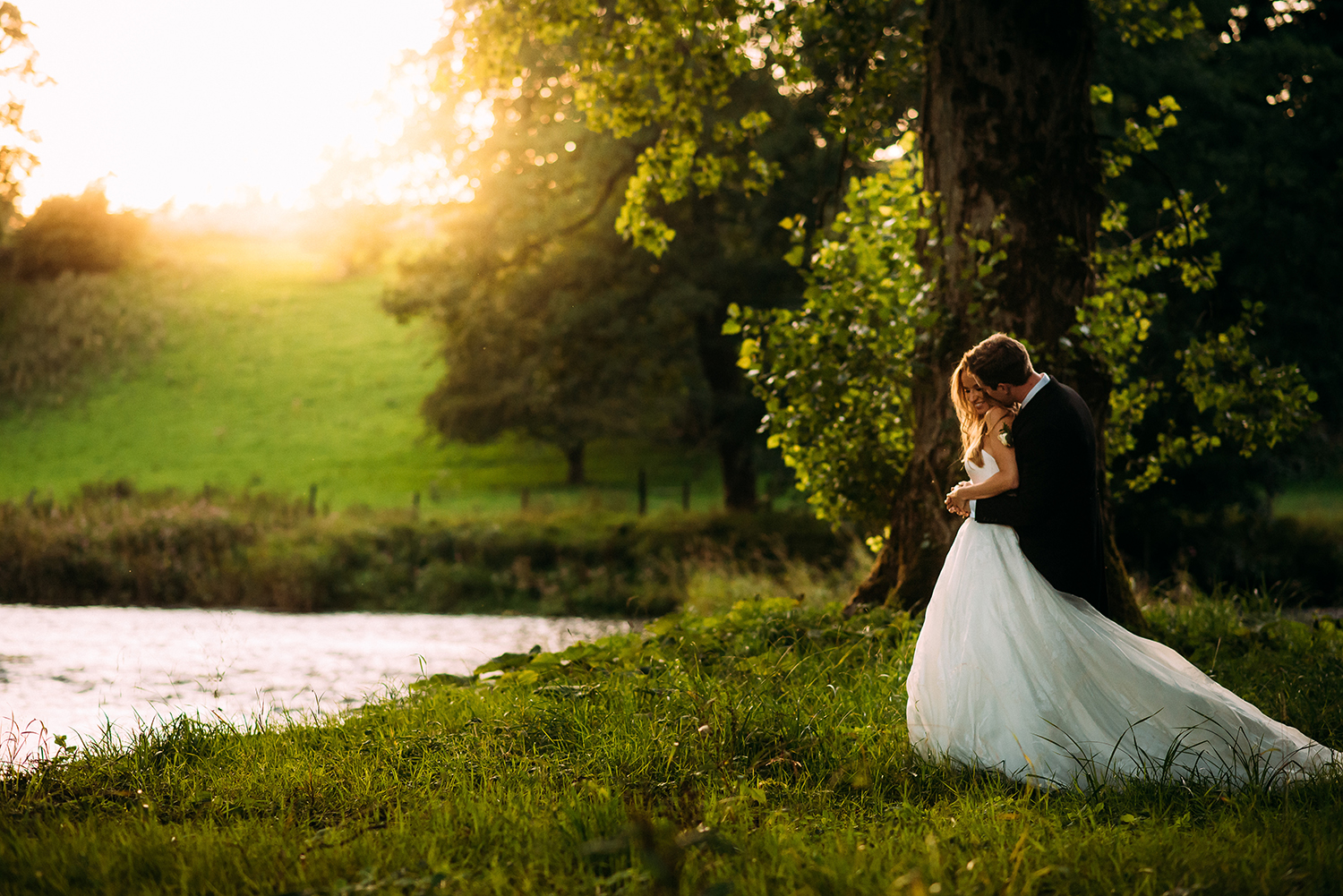 bride and groom cuddle byt the river at sunset