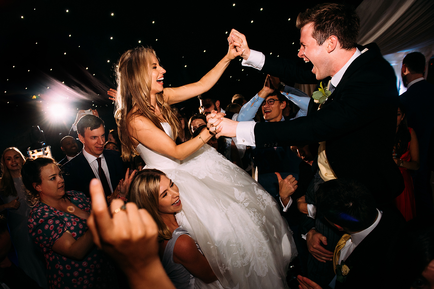  bride and groom holding hands whilst on guests shoulders 