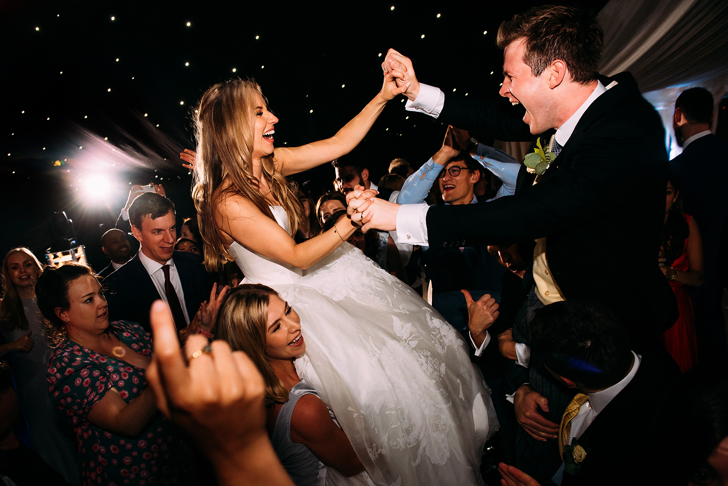 bride and groom holding hands whilst on guests shoulders
