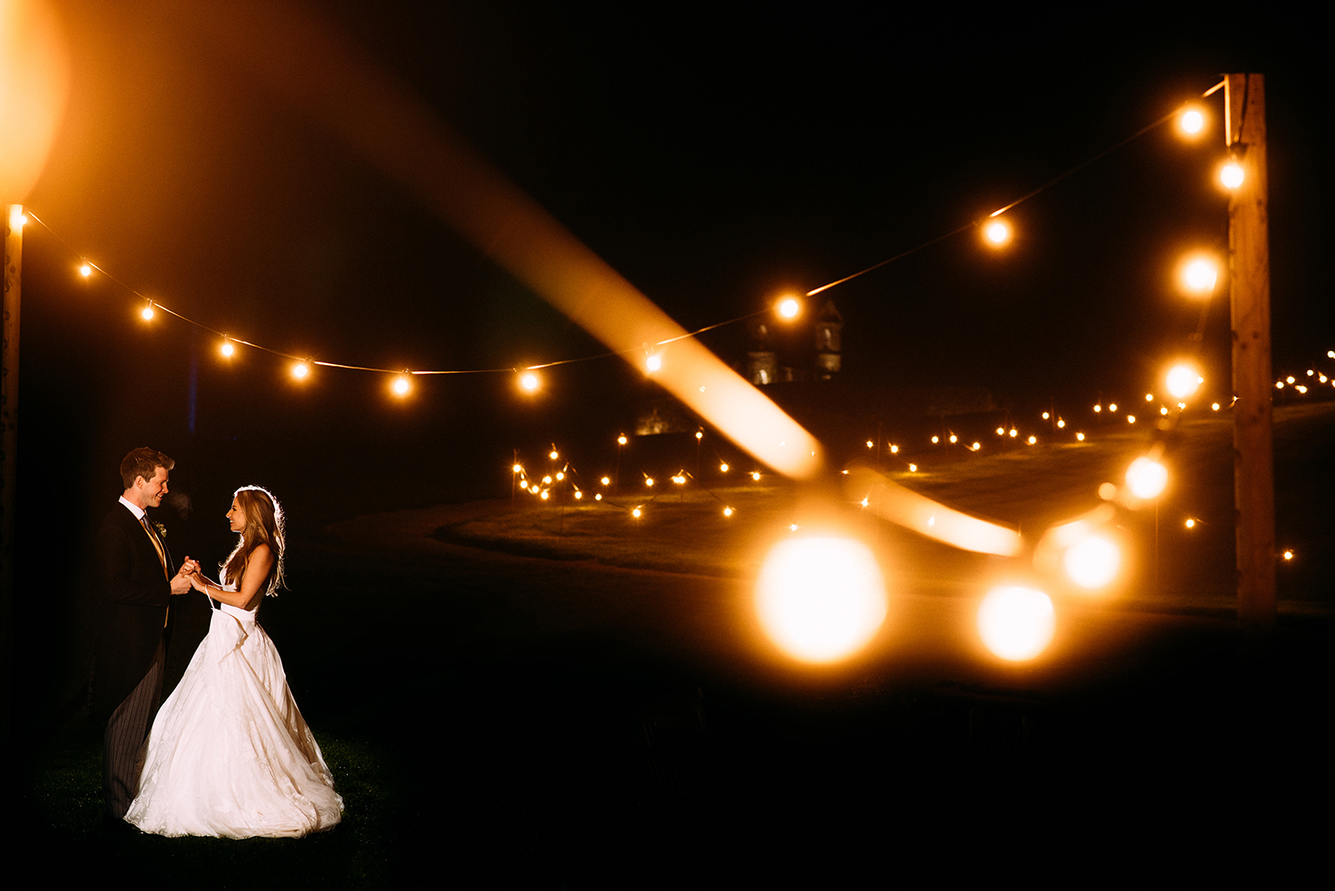off camera flash night time portrait of bride and groom taken through festoon lights