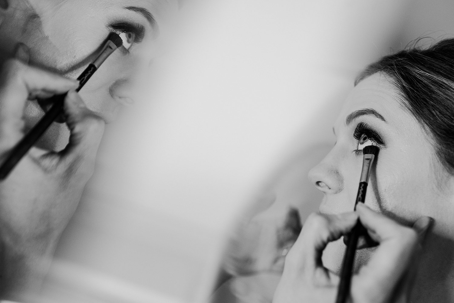 bw photo of bride having eye liner put on with a reflection