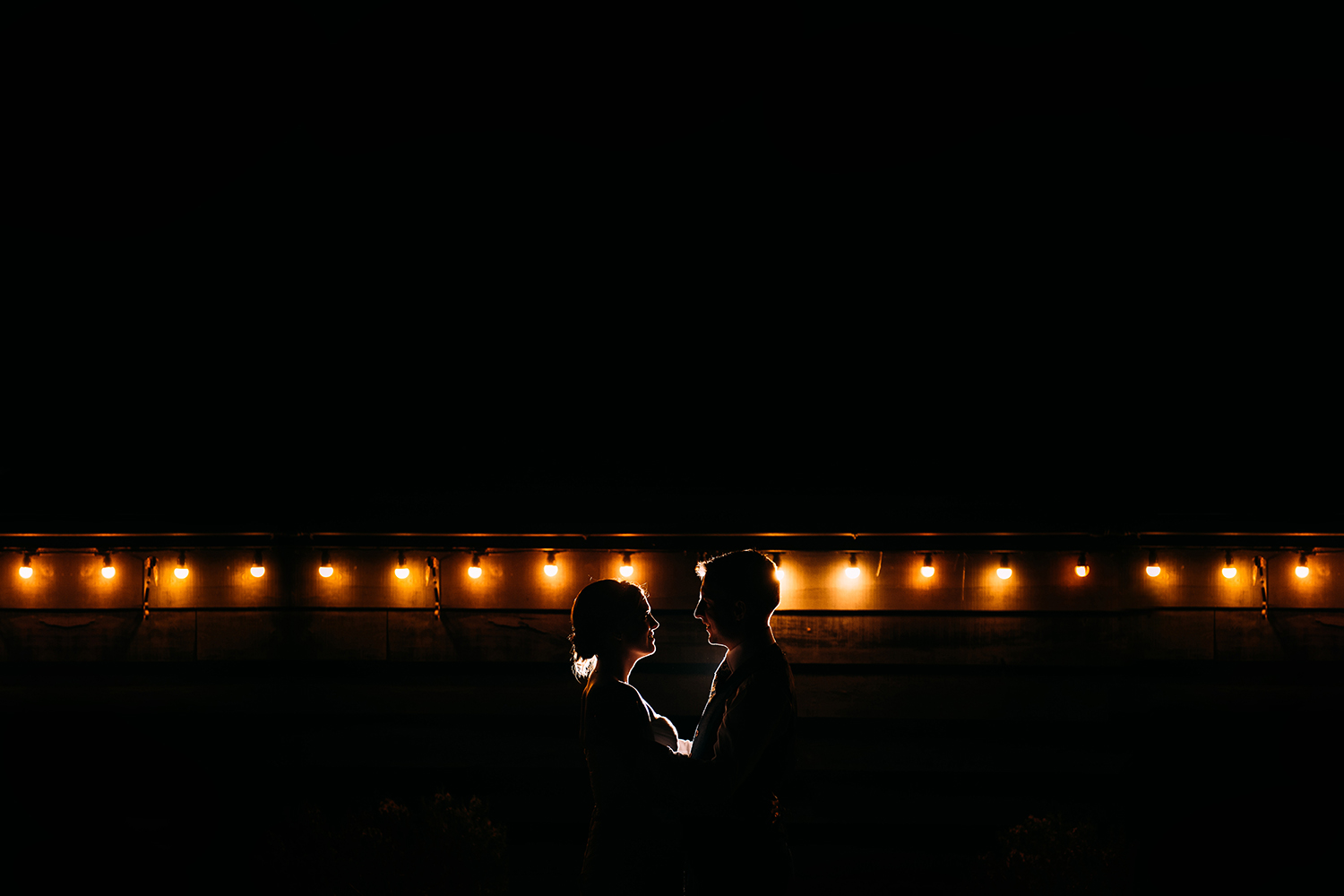 bride and groom night time portrait in front of some light bulbs
