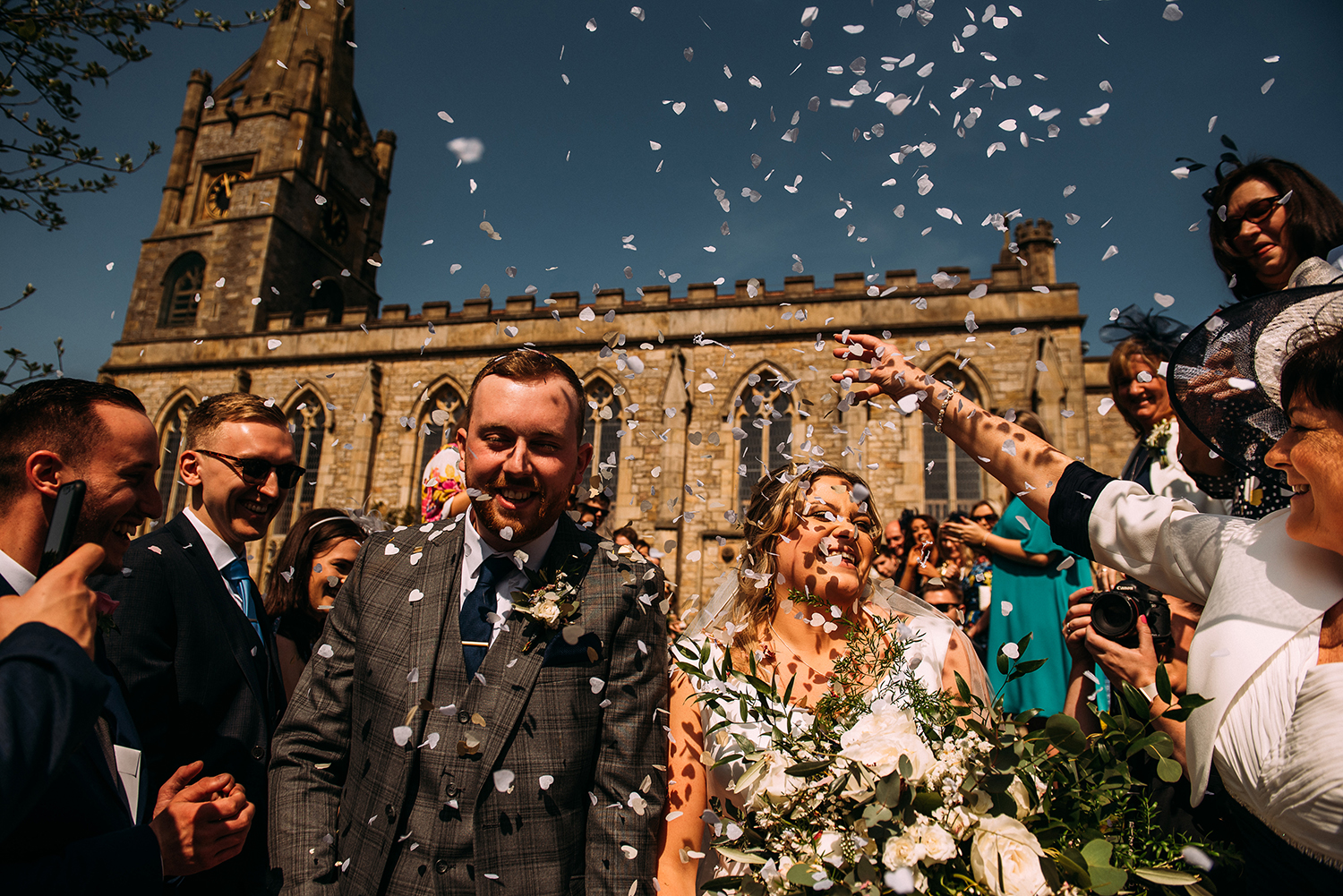 bride and groom walk through confetti outside church