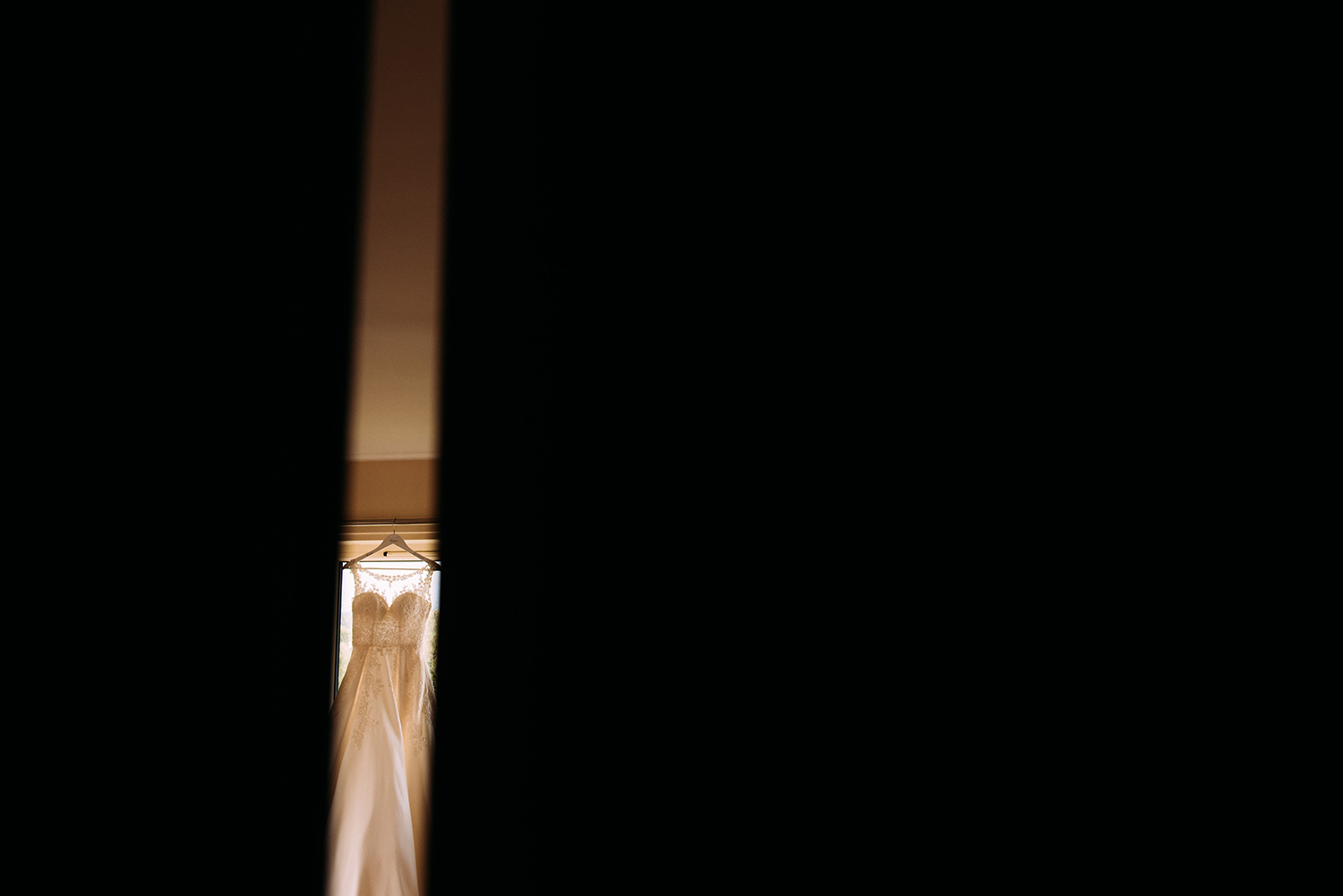 wedding dress hanging up, taken through a gap in the door