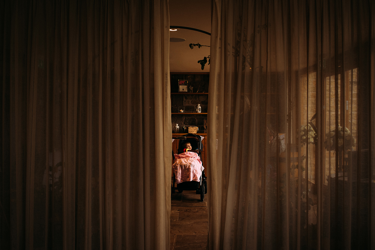 baby in a pram, framed in the centre of the image by a gap in the curtains