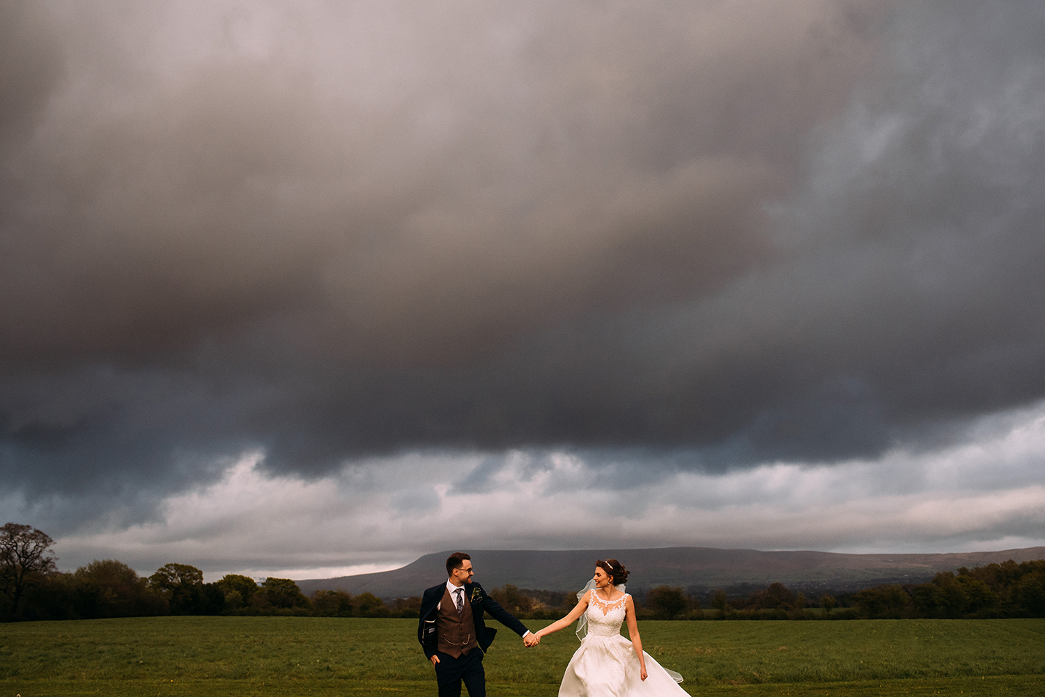 Bride and groom walking up the fields at the Out Barn with Pendle hill in the background.