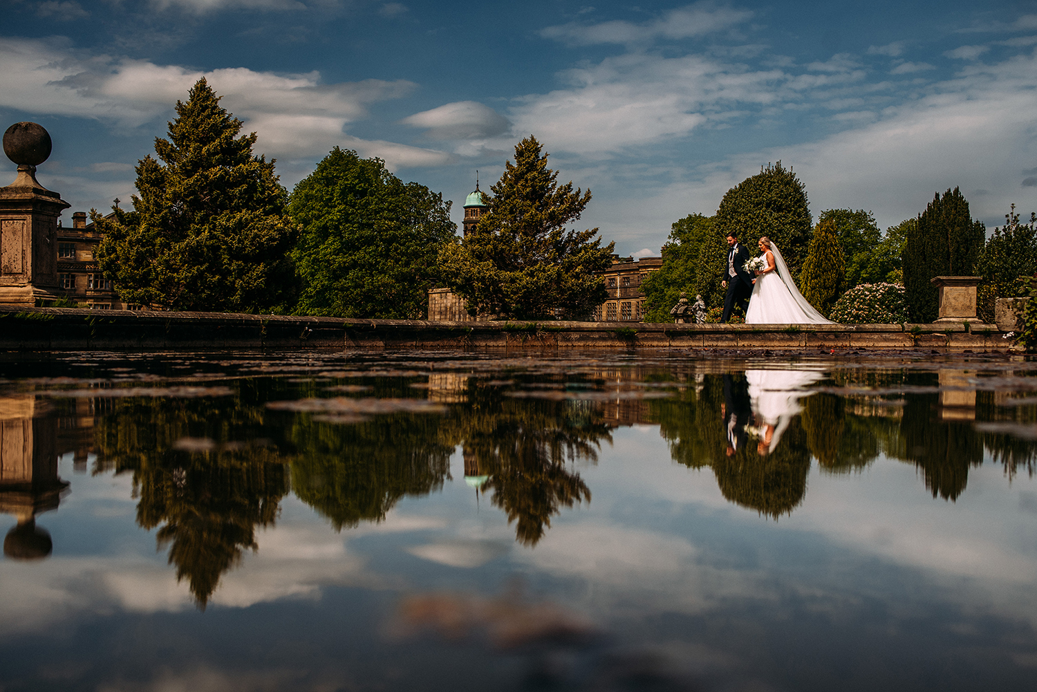 bride and groom walk around a large pond