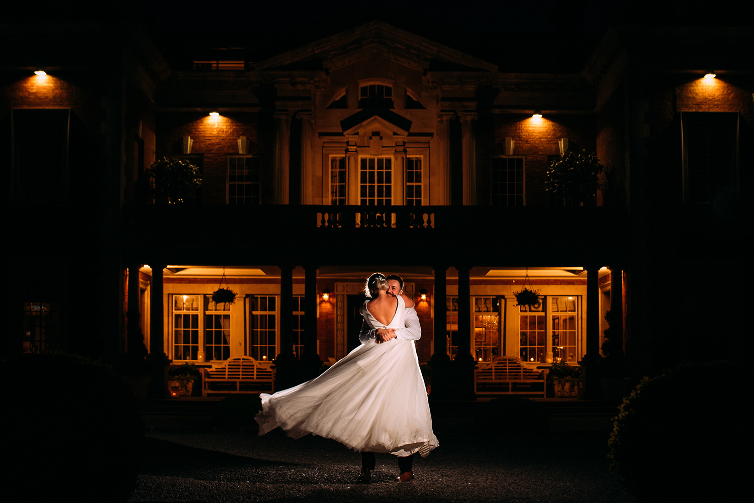 bride and groom hug and spin in front of Eaves hall at night