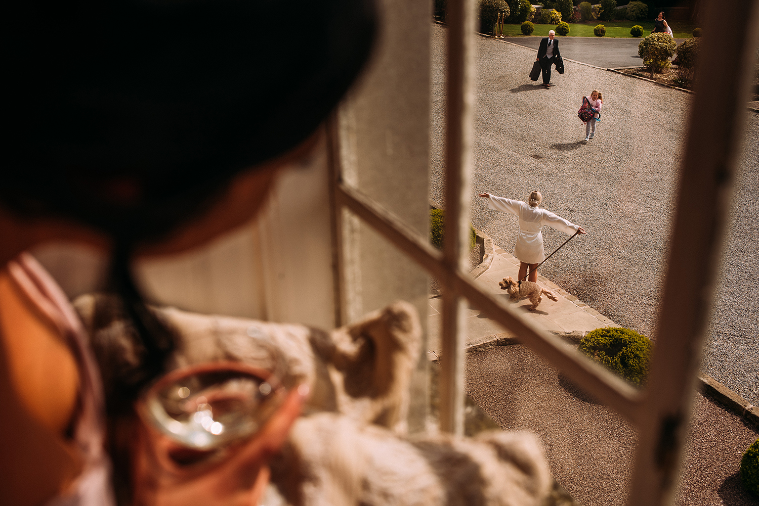 bridesmaid looks out of the window of Eaves hall at the bride hugging her friend down below