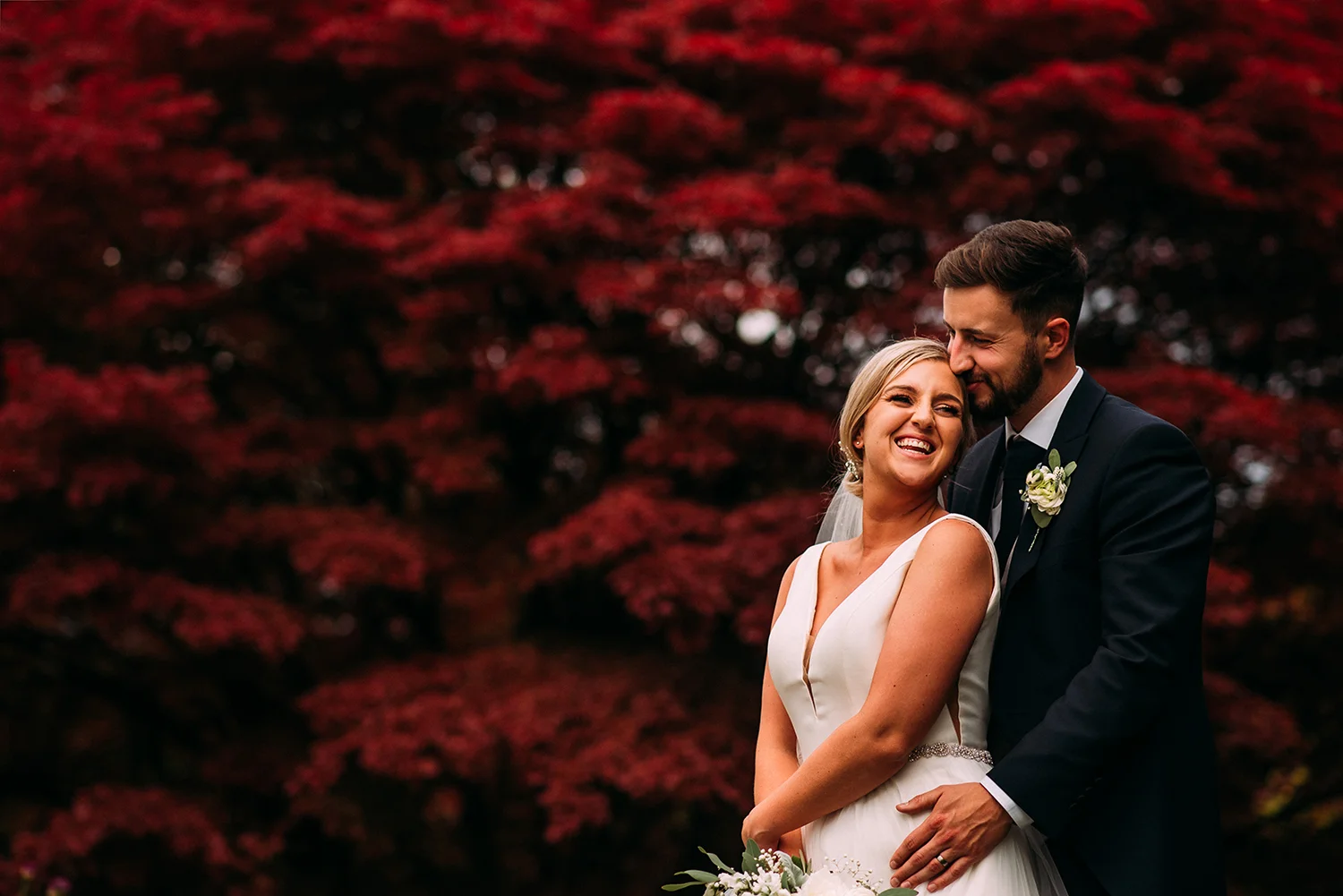 bride and groom in front of the red leaves at Eaves hall