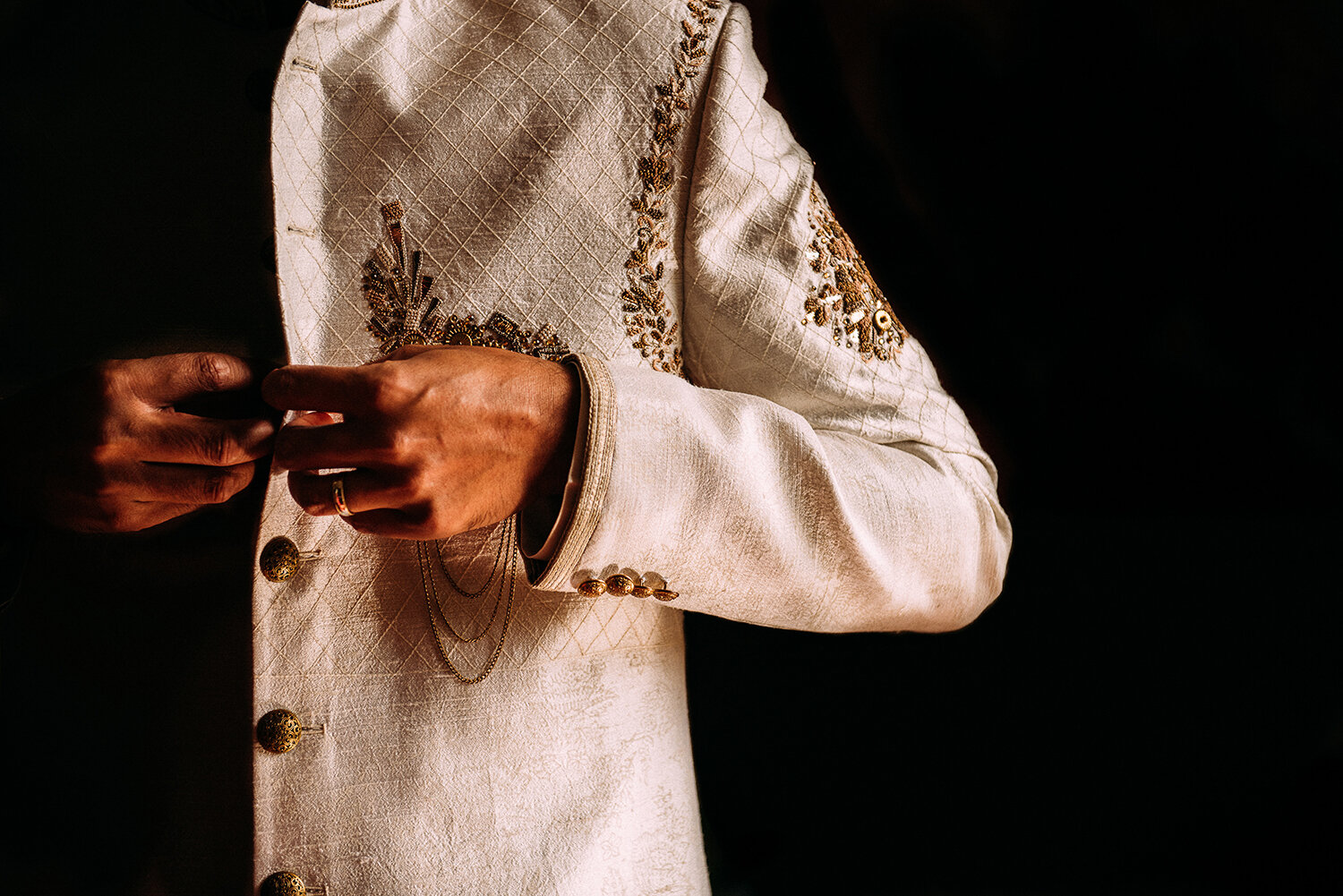  groom fastening buttons on traditional Indian wedding jacket 