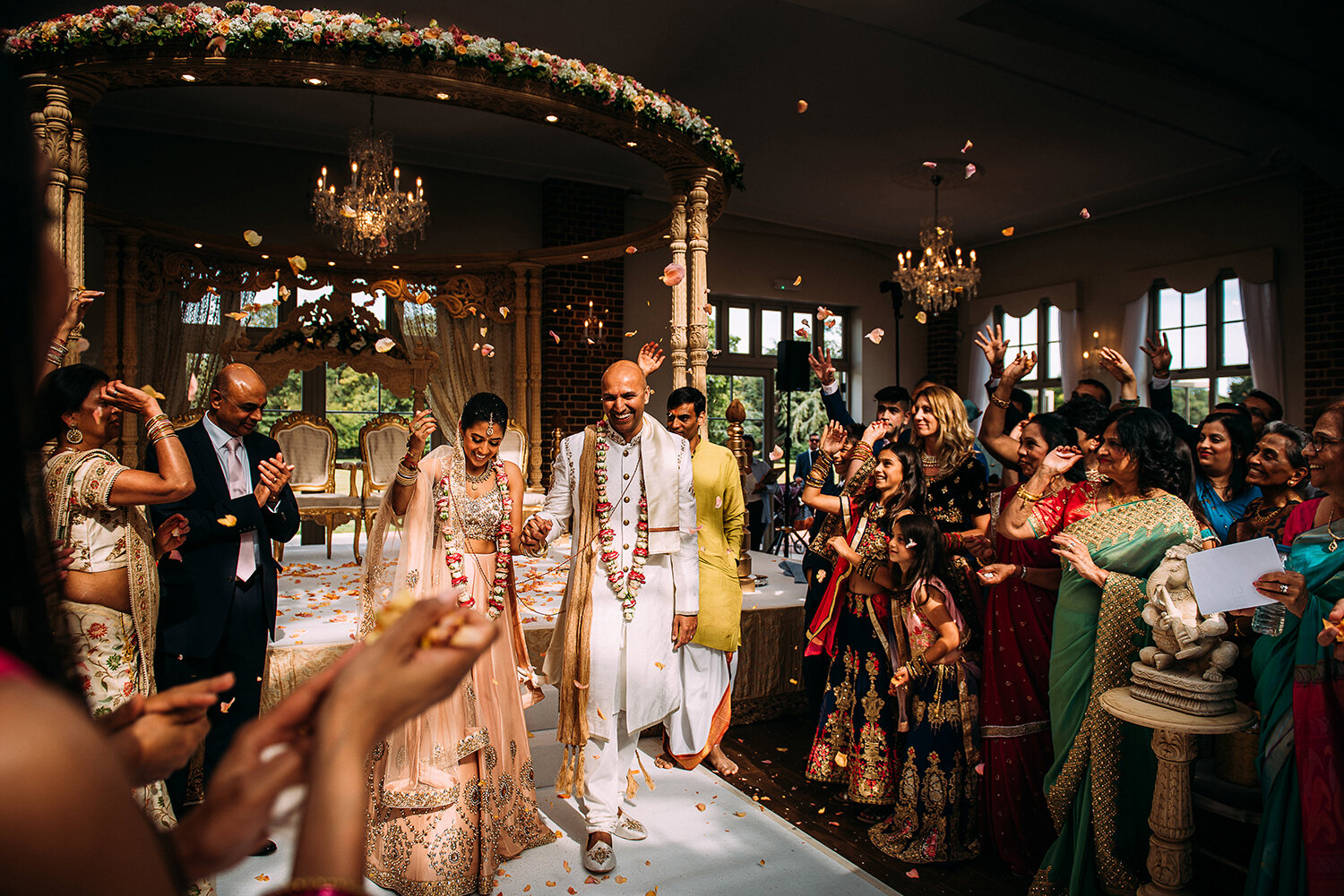  busy wide scene of the bride and groom walking out of the ceremony as flowers are thrown on them 