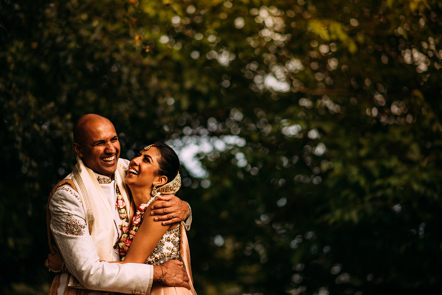  bride and groom laughing and hugging under a tree 