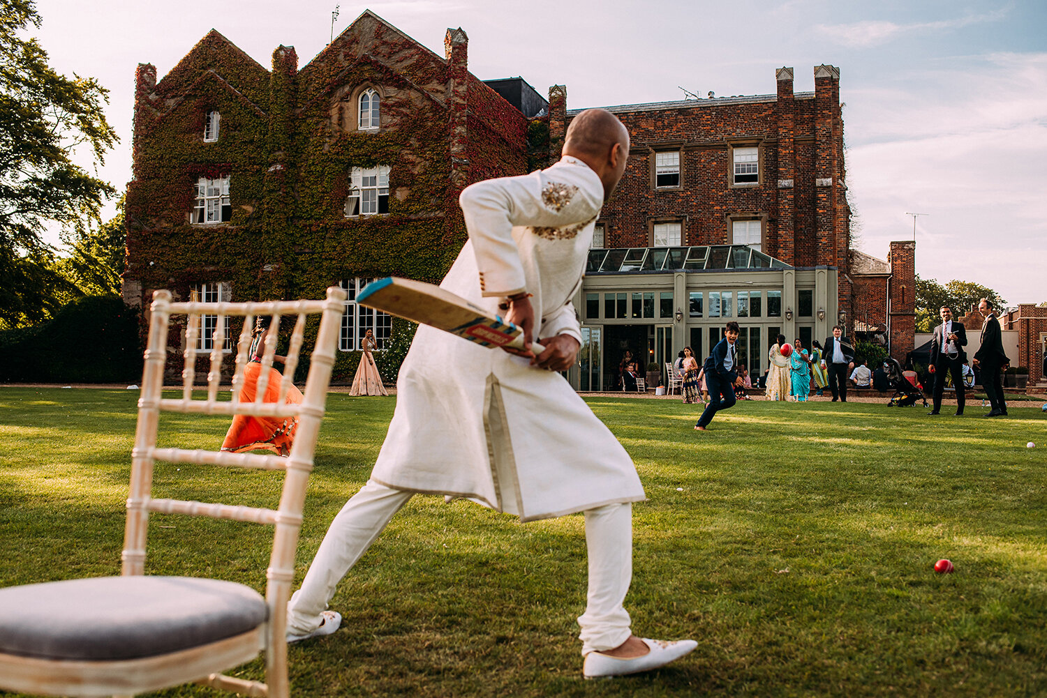  taken from behind the groom as he plays cricket in front of Offley place building 