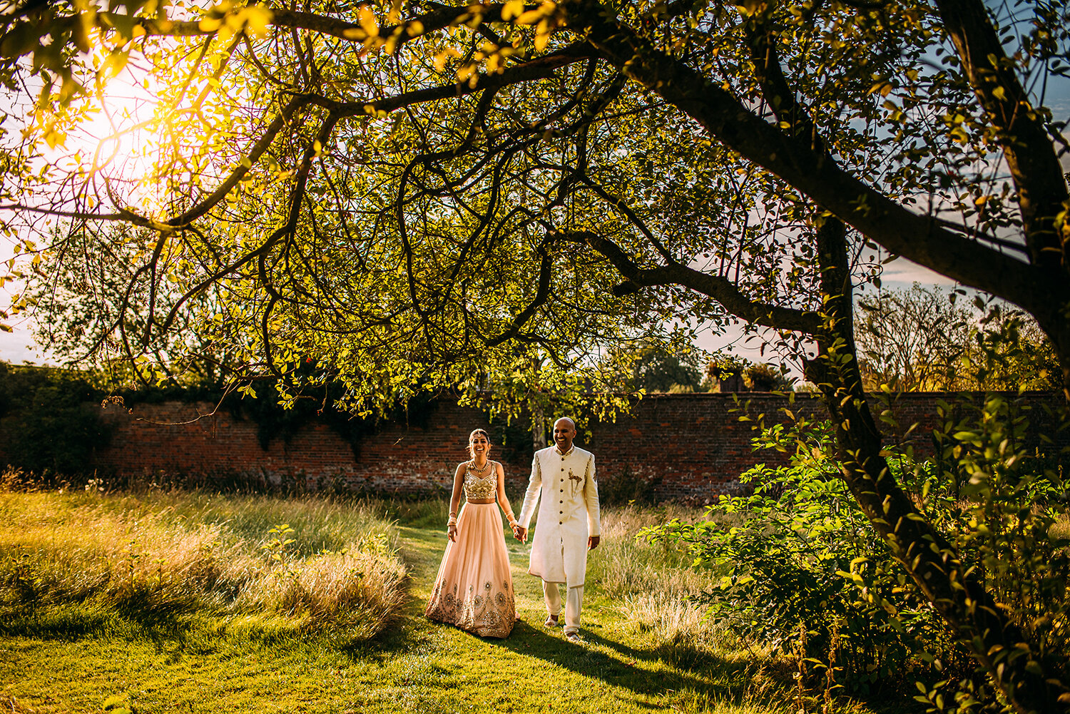  bride and groom walking through the gardens under a tree 