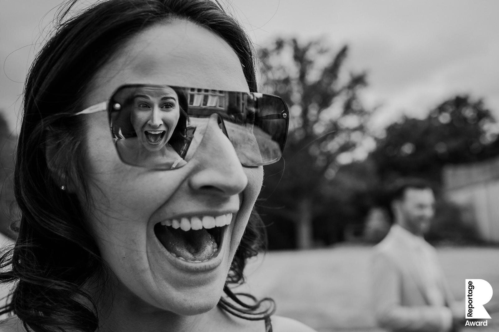  girl laughing at her twin who you can see the reflection of in her glasses. 