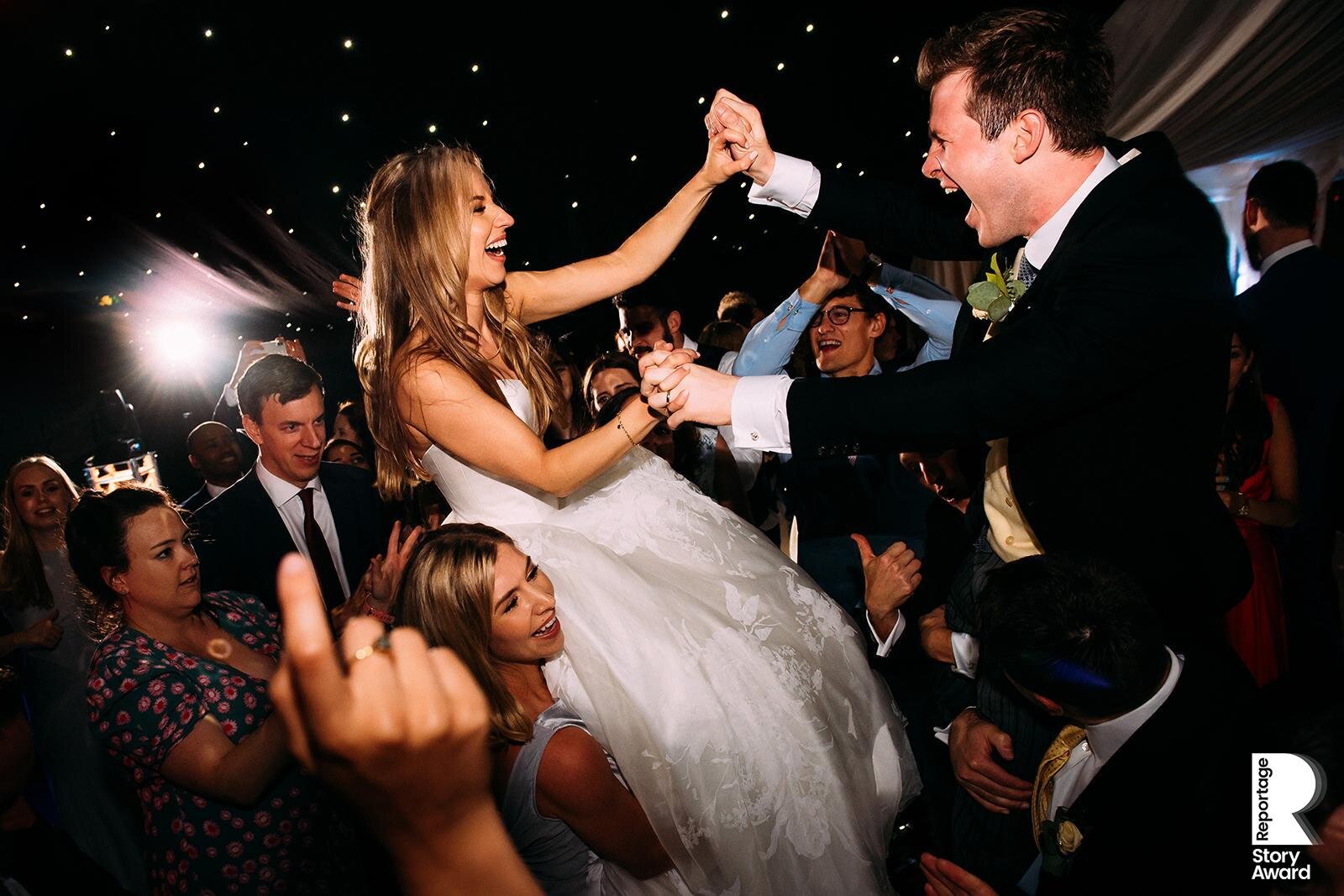  Bride and groom lifted by friends on a busy dance floor 