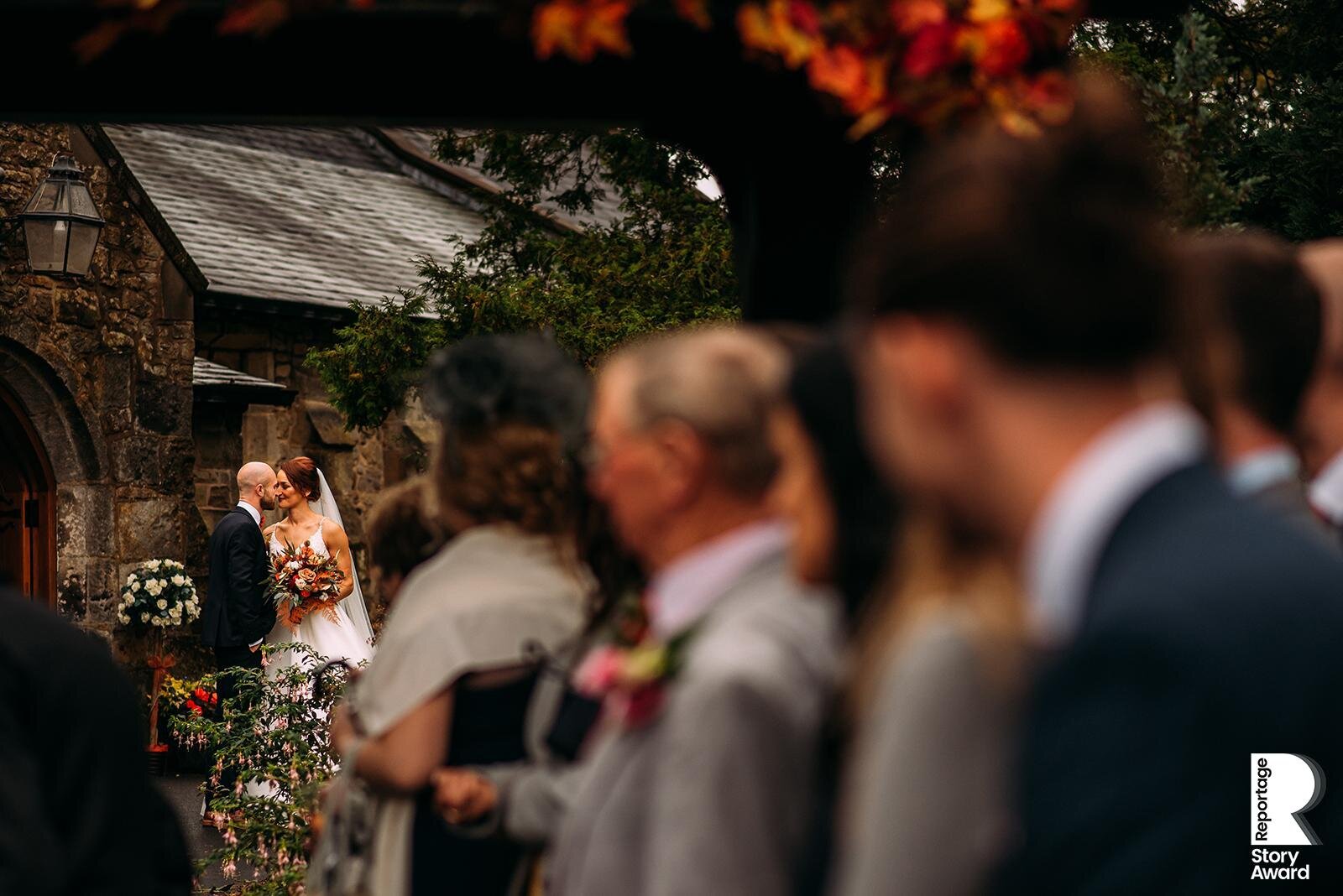 Bride and groom kiss as their guests wait to throw confetti on them. 