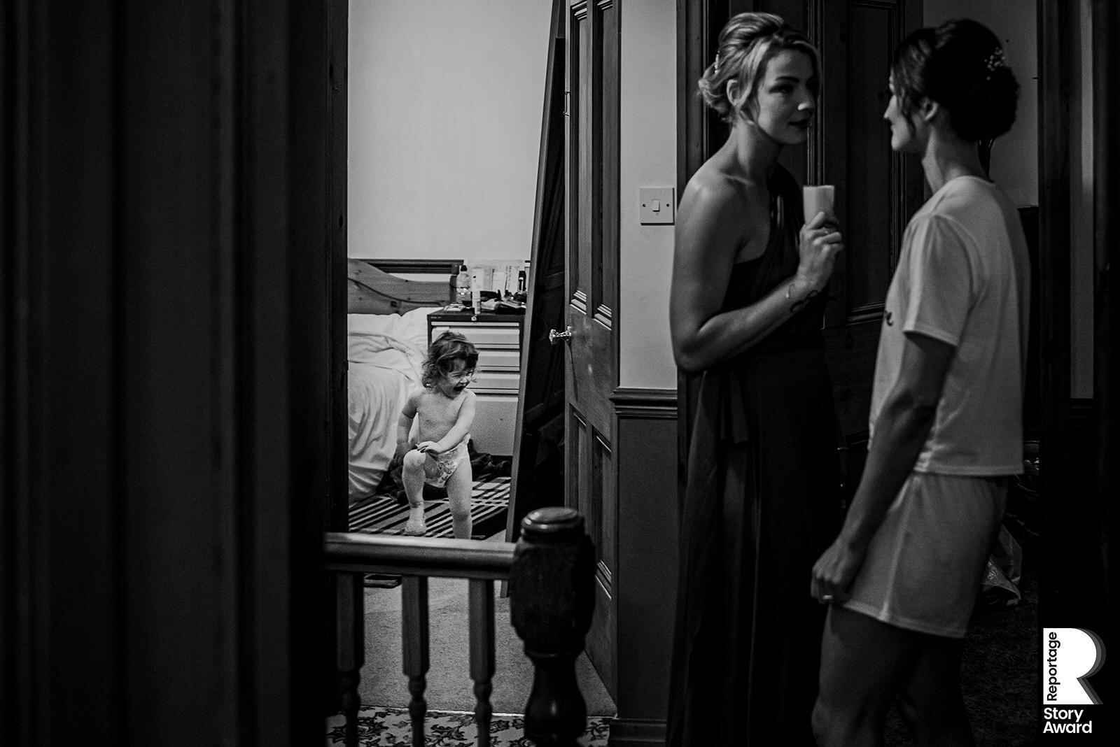  bride and sister talking while her daughter dances in the mirror. 