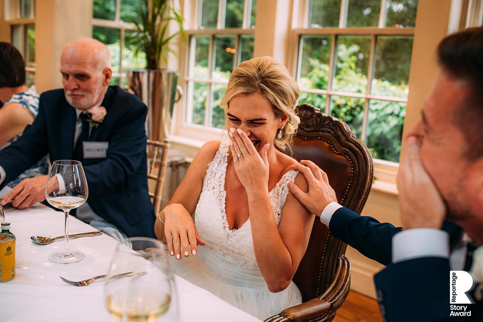  Groom has his hand on brides shoulder as they laugh at a trick played on her father. 