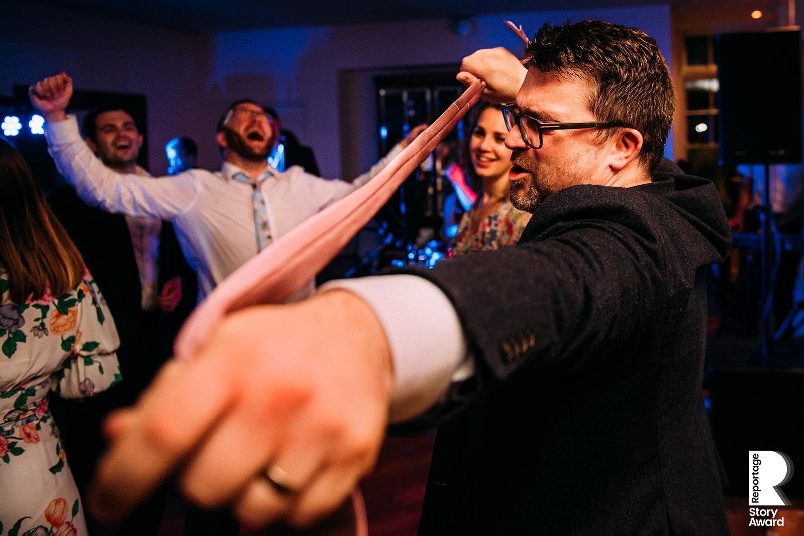  Man plays with tie while another cheers on the dance floor. 