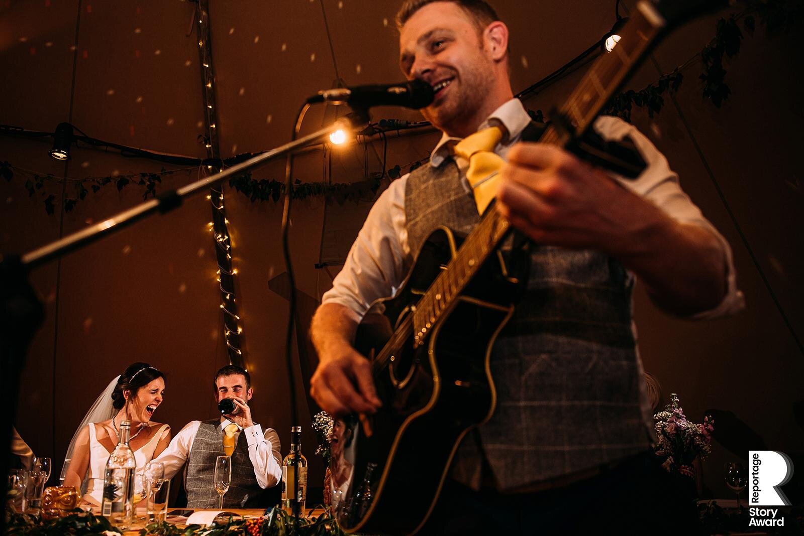  Bride and groom laughing at best man song on guitar. 