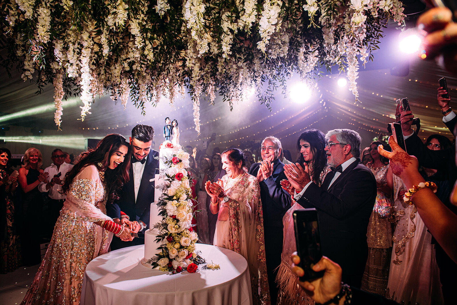  Bride and groom cutting cake under huge amount of flowers. 