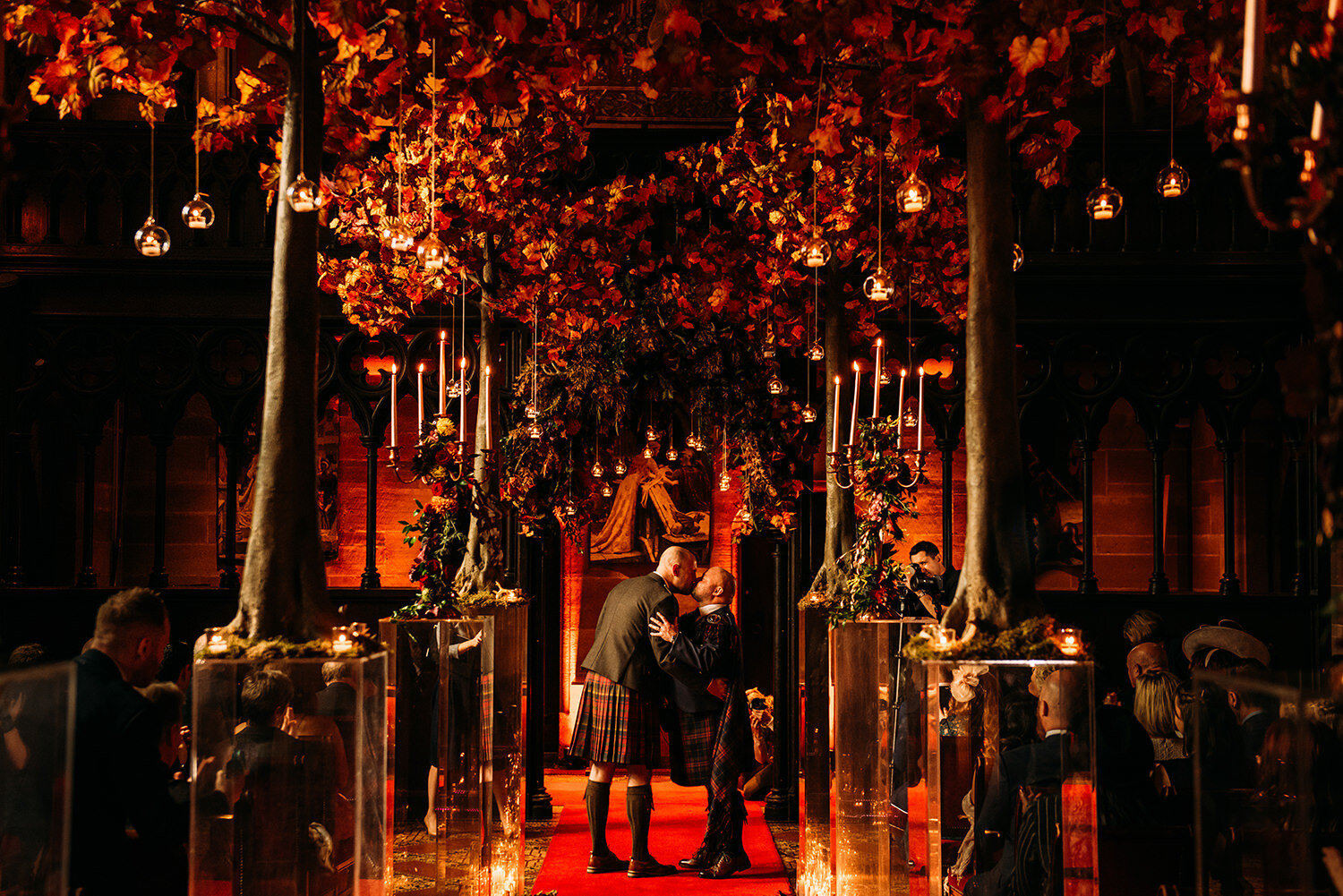  Two grooms kiss in the ceremony under autumnal trees 